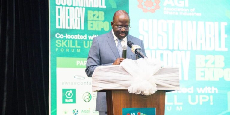 Man in a blue suit speaks at a podium with microphone during a conference; bold teal backdrop says 'Sustainable' and 'Energy Expo' behind him.