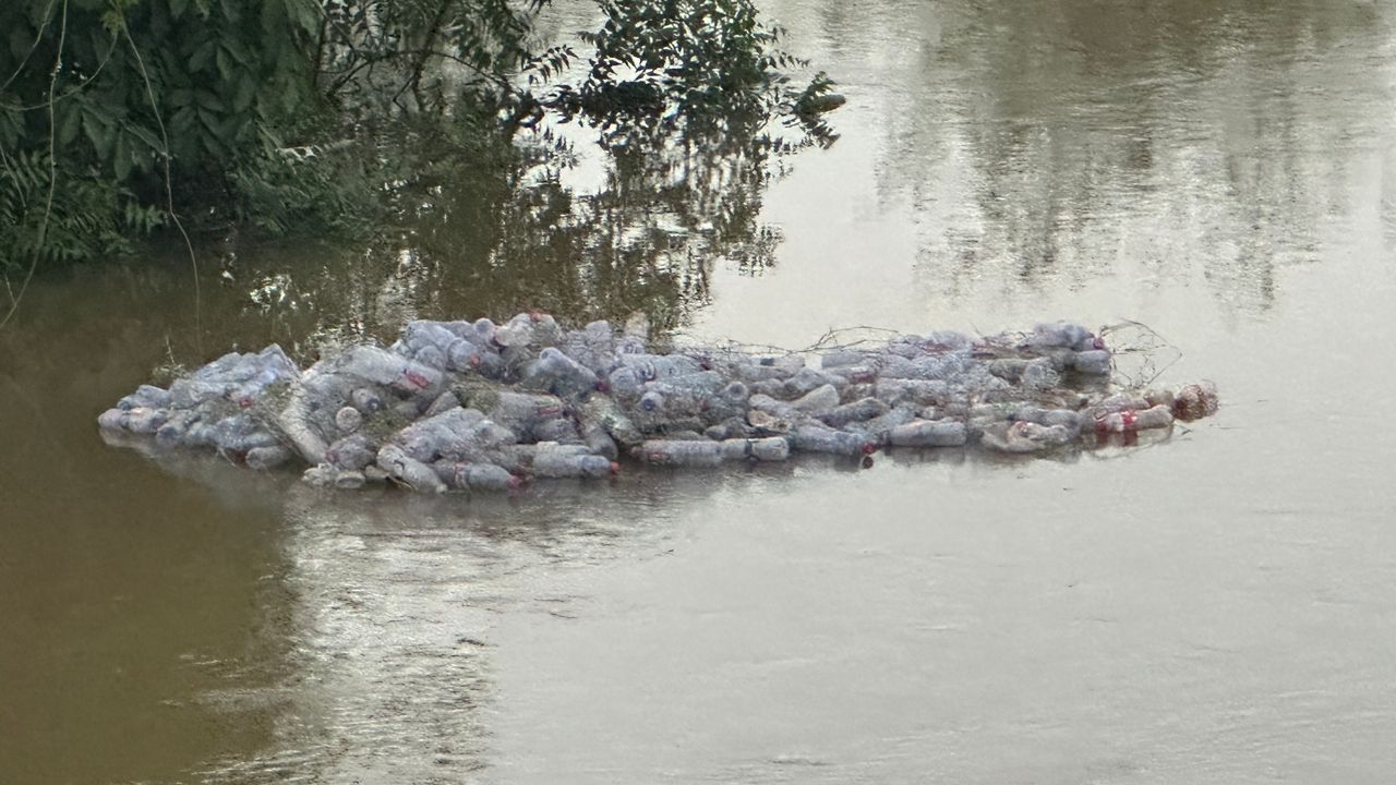 WhatsApp-Image-2026-05-28-at-074502 | Ghanaguardian.com Floating pile of plastic bottles and debris in a river near overhanging trees, showing water pollution artefact on the surface.