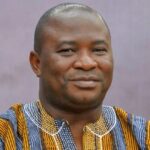 Portrait of a smiling man wearing a colorful striped traditional African shirt against a muted purple background.