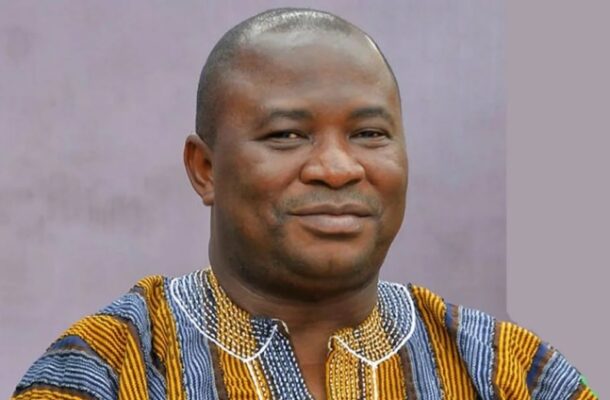 Portrait of a smiling man wearing a colorful striped traditional African shirt against a muted purple background.