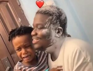 A smiling man comfortingly hugs a crying child near a door, with a red heart emoji above the man's head.