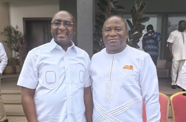 Two men in light-colored outfits smile for the camera at an outdoor event.