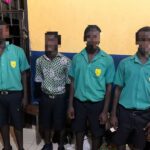 Four male students in green uniforms with crest badges stand indoors; one wears a patterned shirt and all faces are pixelated for privacy.