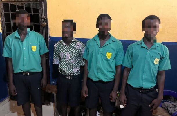 Four male students in green uniforms with crest badges stand indoors; one wears a patterned shirt and all faces are pixelated for privacy.
