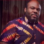 Man with a beard wearing a purple, orange, and yellow tie-dye shirt indoors.