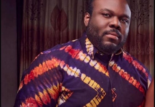 Portrait of a man with a beard wearing a purple shirt with orange and yellow diagonal stripes.