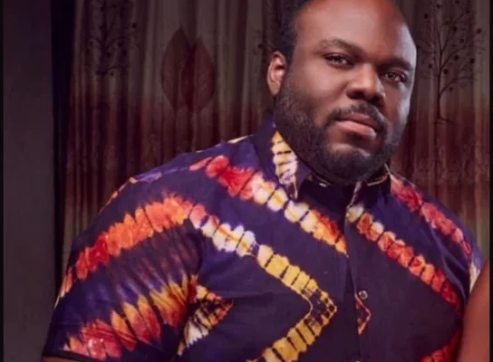 Man with a beard wearing a purple, orange, and yellow tie-dye shirt indoors.