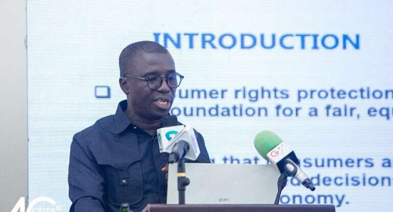 Man with glasses speaking at a podium with a laptop and two microphones, a slide behind him reads 'INTRODUCTION'.