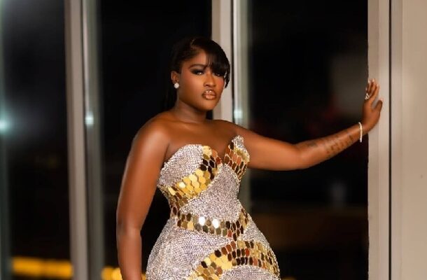 Woman in a silver and gold sequined gown posing by a doorway at night.