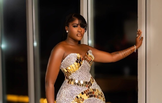 Woman in a silver and gold sequined gown posing by a doorway at night.