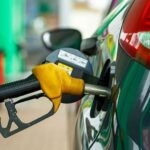 Close-up of a yellow gas pump nozzle fueling a green car at a gas station.