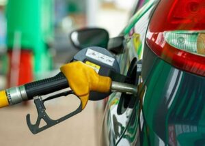 Close-up of a yellow gas pump nozzle fueling a green car at a gas station.