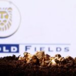 Miniature figurine miner digging in soil with gold nuggets scattered, Gold Fields logo in the background.