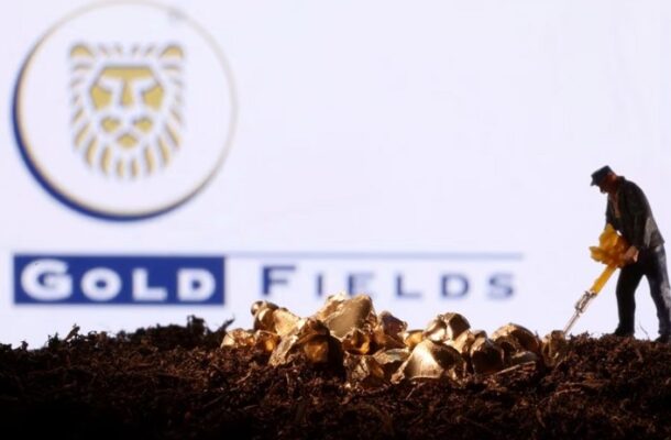 Miniature figurine miner digging in soil with gold nuggets scattered, Gold Fields logo in the background.