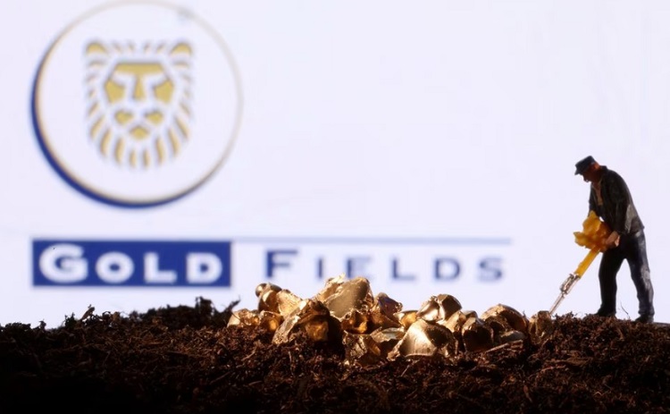 Miniature figurine miner digging in soil with gold nuggets scattered, Gold Fields logo in the background.