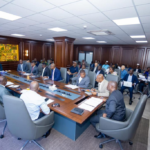 A formal meeting in a wood-paneled conference room with officials around a long table, Ghanaian flags visible, Ministry of Finance seal in the corner.