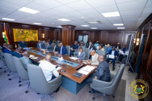 A formal meeting in a wood-paneled conference room with officials around a long table, Ghanaian flags visible, Ministry of Finance seal in the corner.