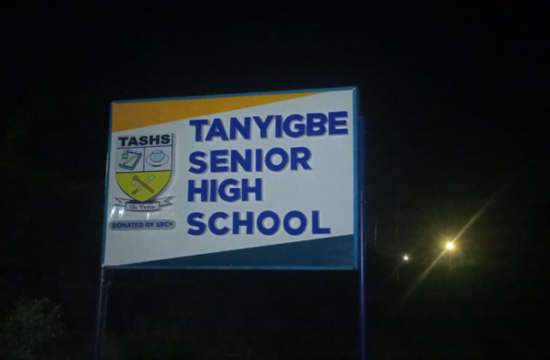 Night photo of a sign for Tanyigbe Senior High School with a crest on the left side? (Note: remove question mark)