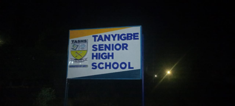 Night photo of a sign for Tanyigbe Senior High School with a crest on the left side? (Note: remove question mark)