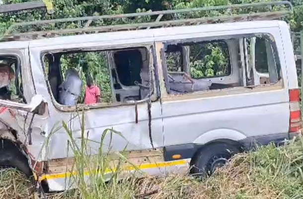 White van heavily damaged with front end crushed, drivers side on grassy ditch amid tall weeds and water nearby; appears abandoned after an accident