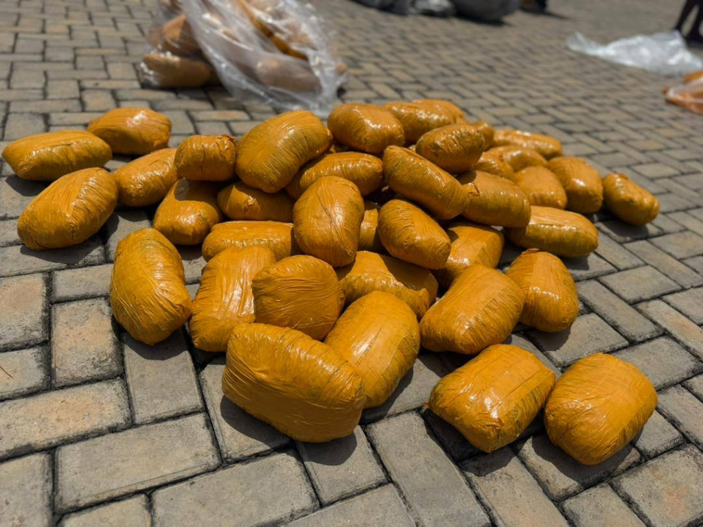 Pile of orange-wrapped bundles on a brick-paved ground.