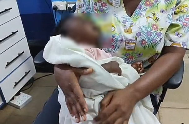 Healthcare worker in a floral top cradling a newborn wrapped in white cloth in a medical room.
