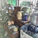 Smoke-damaged, cluttered kitchen counter with burnt containers, a large metal pot, and charred debris after a fire