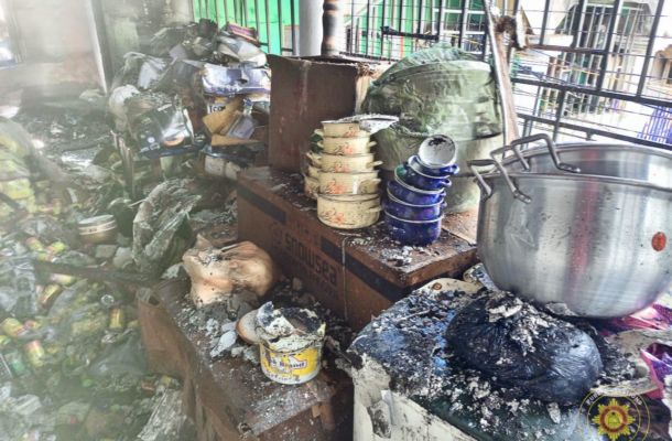 Smoke-damaged, cluttered kitchen counter with burnt containers, a large metal pot, and charred debris after a fire