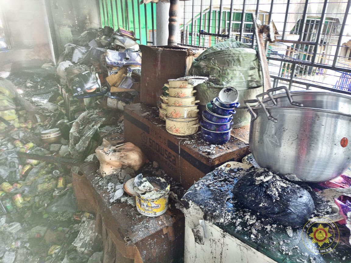 Smoke-damaged, cluttered kitchen counter with burnt containers, a large metal pot, and charred debris after a fire
