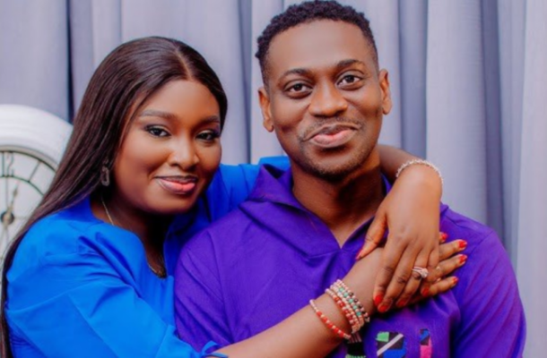Couple posing closely, woman in blue wrapping her arm around a man in purple, both smiling at the camera in a cozy hug.