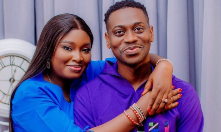 Couple posing closely, woman in blue wrapping her arm around a man in purple, both smiling at the camera in a cozy hug.