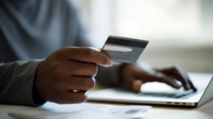Person holds a credit card while typing on a laptop, suggesting online shopping or payment.