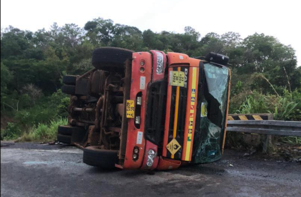 image-684 | Ghanaguardian.com Orange bus overturned on its side on a rural road, with broken windshield and debris nearby.