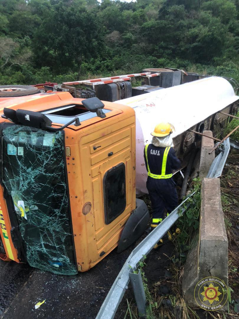 image-686 | Ghanaguardian.com Orange truck tipped onto its side on a highway, with a cracked windshield and a large white tanker trailer, a responder in a helmet nearby