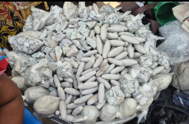 Pile of long, white, cylindrical food items arranged in a mound at a market stall, surrounded by bags and wrapped bundles.
