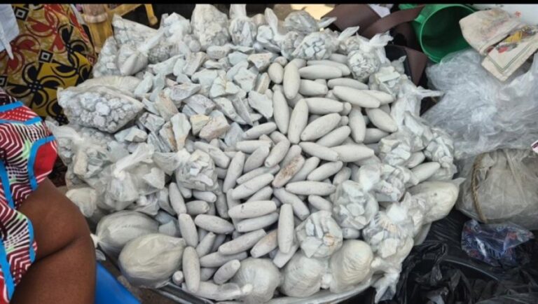 Pile of long, white, cylindrical food items arranged in a mound at a market stall, surrounded by bags and wrapped bundles.