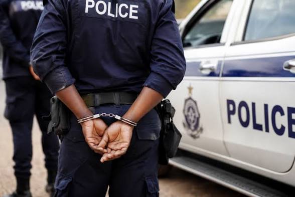 Uniformed police officer with hands cuffed behind back standing beside a police car