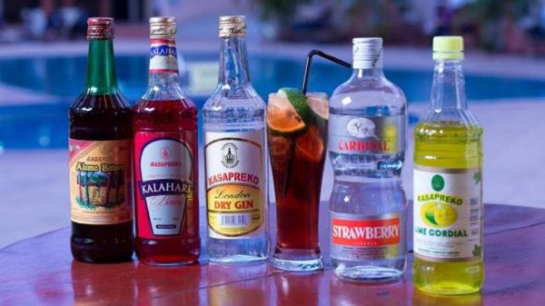 Row of colorful liquor bottles lined up on a poolside table with a glass of mixed drink nearby.