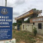 Blue signboard reads 'KNUST SENIOR HIGH SCHOOL (MMADWEMMA)' with address and hours, standing near the entrance gate.