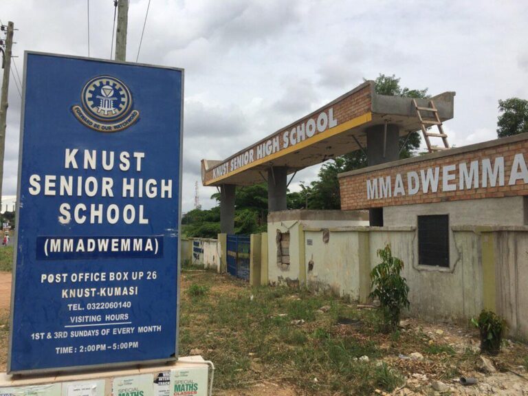 Blue signboard reads 'KNUST SENIOR HIGH SCHOOL (MMADWEMMA)' with address and hours, standing near the entrance gate.