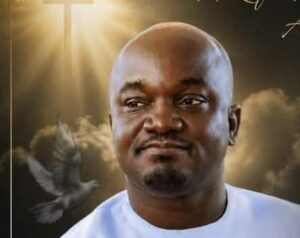 Close-up of a smiling Black man with a shaved head wearing a white shirt, with a dove and sunlit clouds in the background.
