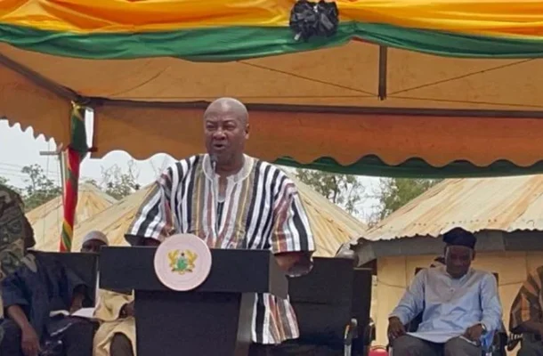 mahama | Ghanaguardian.com A man in a striped shirt speaks at a podium with a seal, under a colorful ceremonial tent, flanked by officials and soldiers.