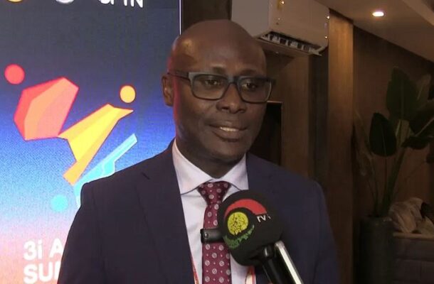 Man in a navy suit and red tie being interviewed, holding a microphone with a TV network logo visible.