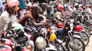 Crowded street scene with numerous motorcycles parked side by side and riders chatting among the bikes.