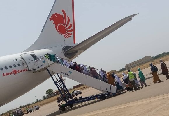 Passengers boarding a Lion Air airplane via mobile stairs on a sunny tarmac.