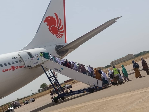 Passengers boarding a Lion Air airplane via mobile stairs on a sunny tarmac.