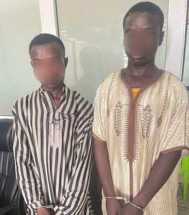 Two men stand side by side indoors with faces blurred for privacy; they wear traditional striped and embroidered robes.