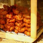 Outdoor wooden display case filled with bags of fried chicken stacked inside on a cloth liner.