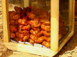 Outdoor wooden display case filled with bags of fried chicken stacked inside on a cloth liner.