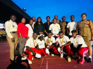 Group of athletes and officials posing with medals and certificates on an outdoor track at dusk/blue hour.